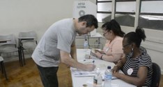 Eleitor assina caderno de votação em mesa receptora de votos com duas mesárias